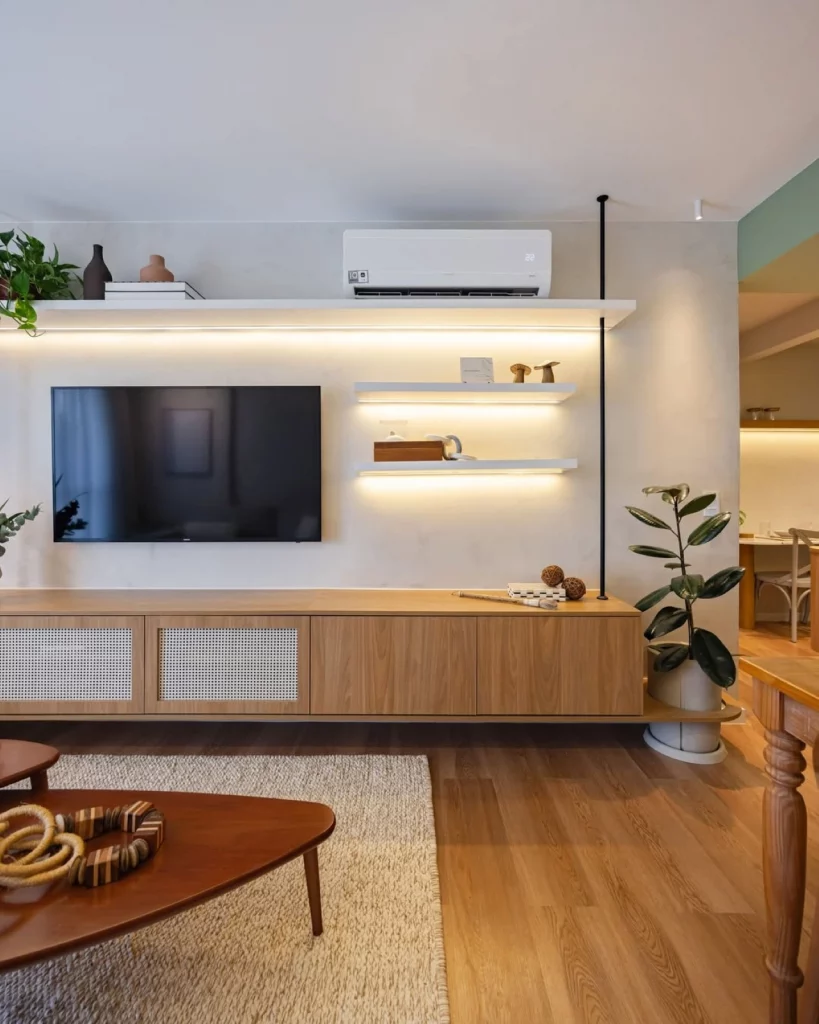 Sala de televisão com prateleiras brancas iluminadas com fita de led na parte inferior, decoradas com plantas e itens decorativos.
