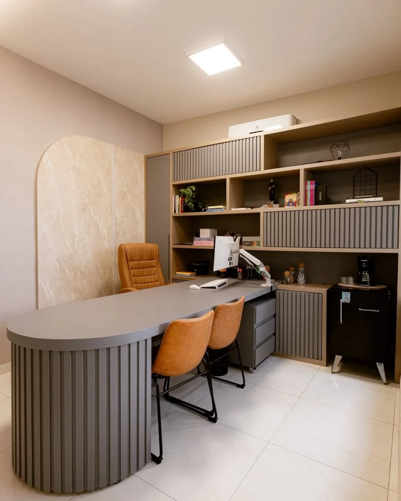 Parede com textura, estantes ao lado e objetos decorativos, mesa cinza e cadeiras marrom caramelo.