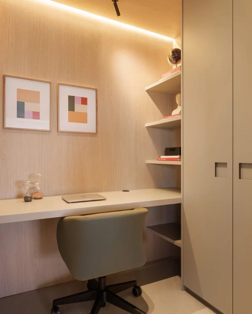 Home office com parede amadeirada, iluminação amarela em fita de LED, dupla de quadros coloridos de frente para a mesa, prateleira lateral.
