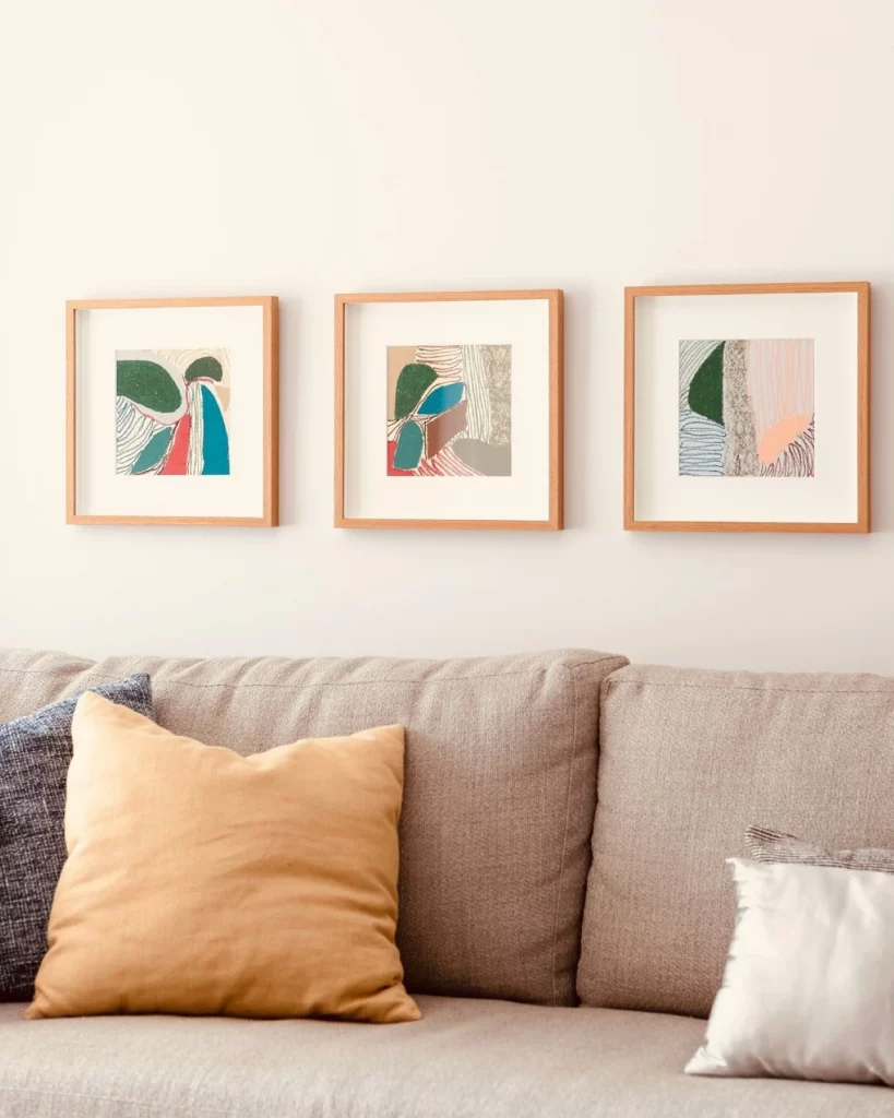 Trio de quadros coloridos e com formas geométricas que enfeitam a sala de estar junto de um sofá cinza amarronzado