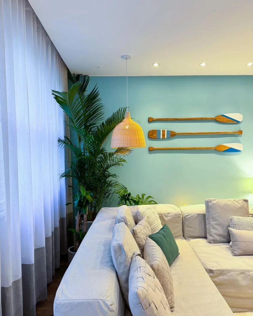 Parede azul decorada com três remos e spots de luz, na frente há um sofá acizentado com almofadas