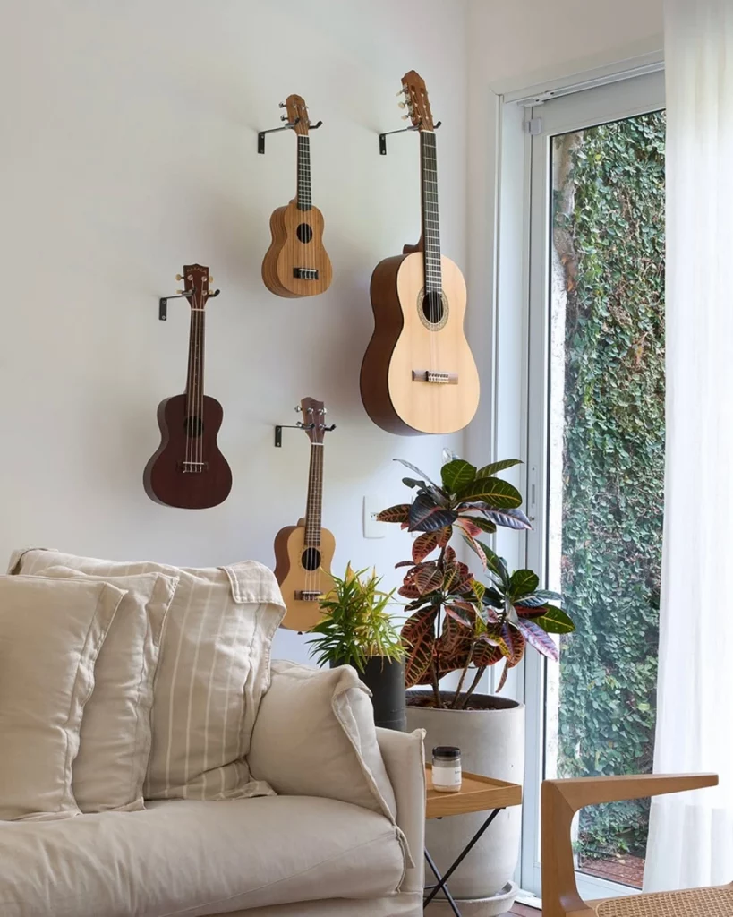 Parede branca decorada com quatro instrumentos musicais, sofá branco com almofadas e vaso grande com planta.
