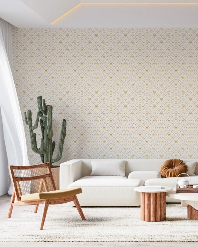 Sala com papel de parede delicado e dourado, com sofá branco, cacto ao fundo e poltrona de madeira