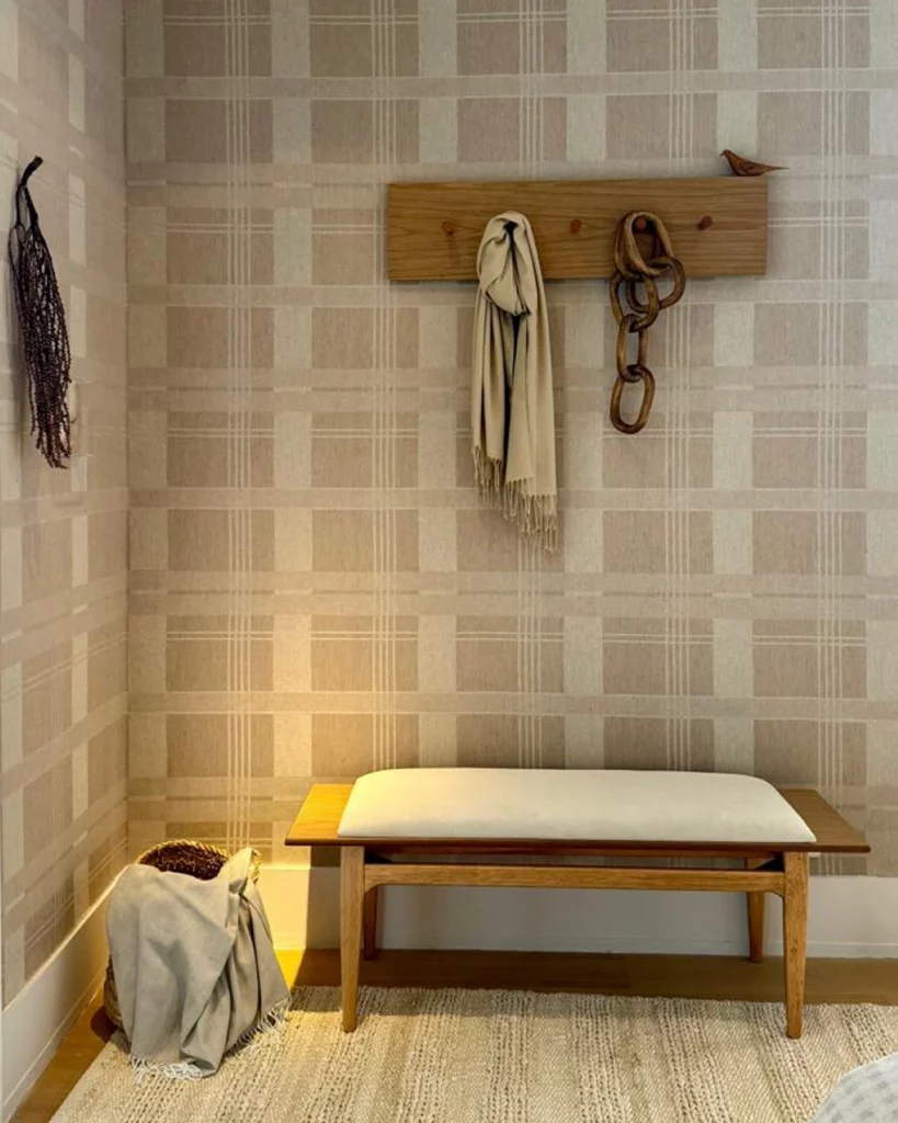 Cantinho de casa com papel de parede xadrez em tons de bege, visual rústico e elegante com banquinho branco e ganchos de madeira