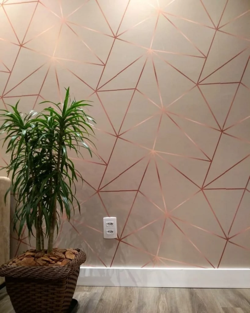 Parede com estampa geométrica em tons de rose gold, com planta no canto e visual moderno