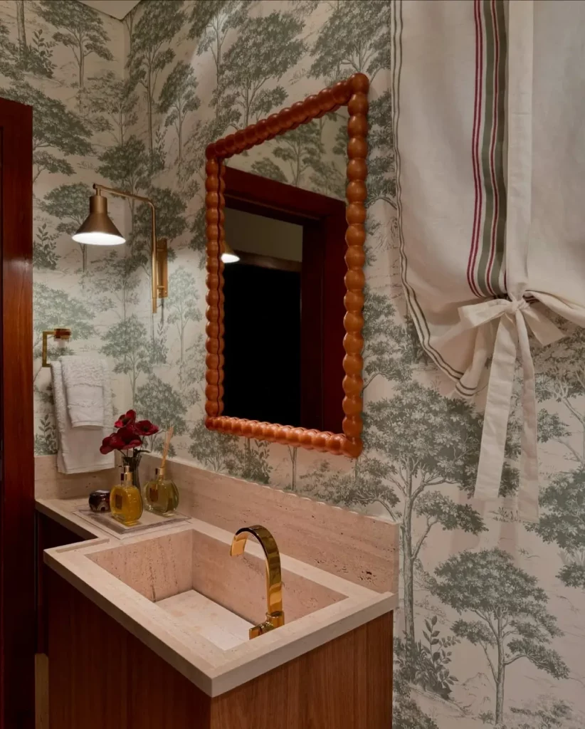 Lavabo com papel de parede de árvores verdes, estilo vintage, com espelho de moldura de bolinhas amarronzadas, cortina vintage com laço.
