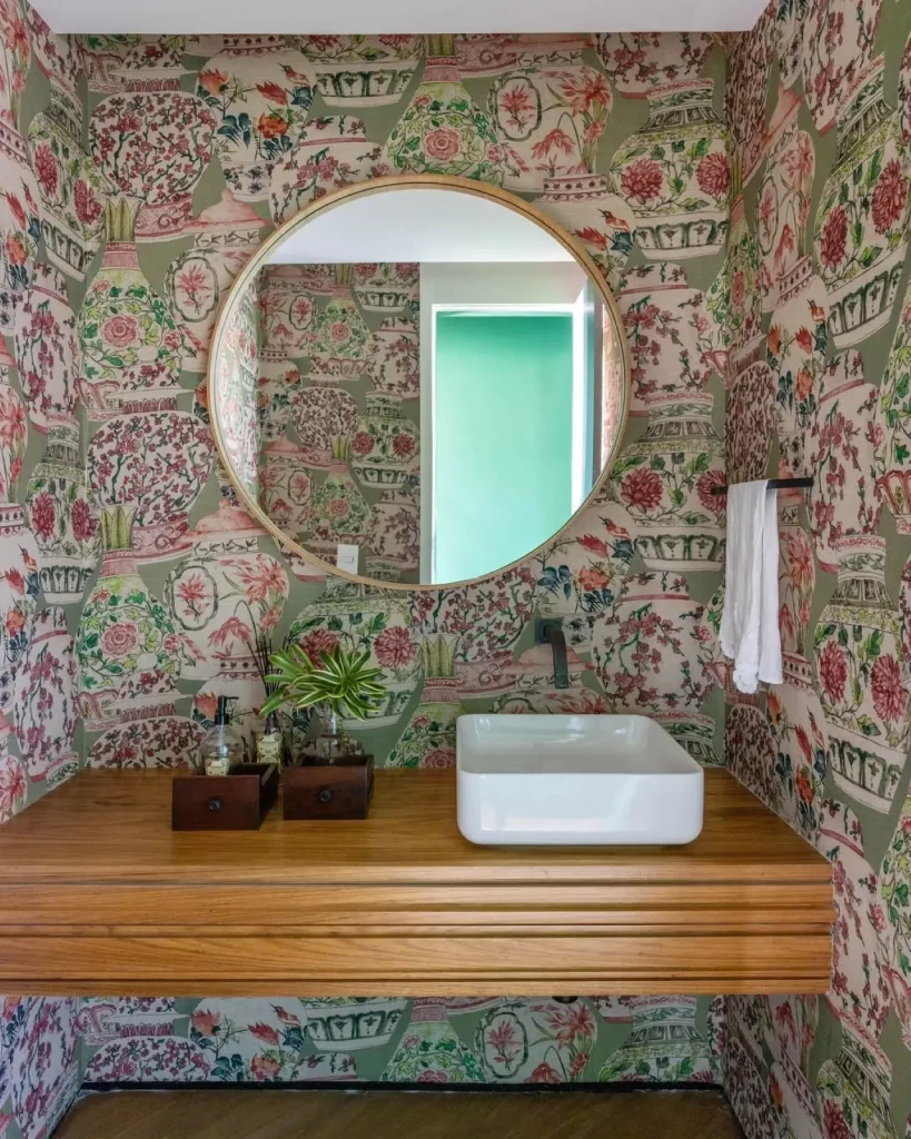 Lavabo com estampa de vasos coloridos, espeçlho redondo e vasos em cima da bancada da pia.