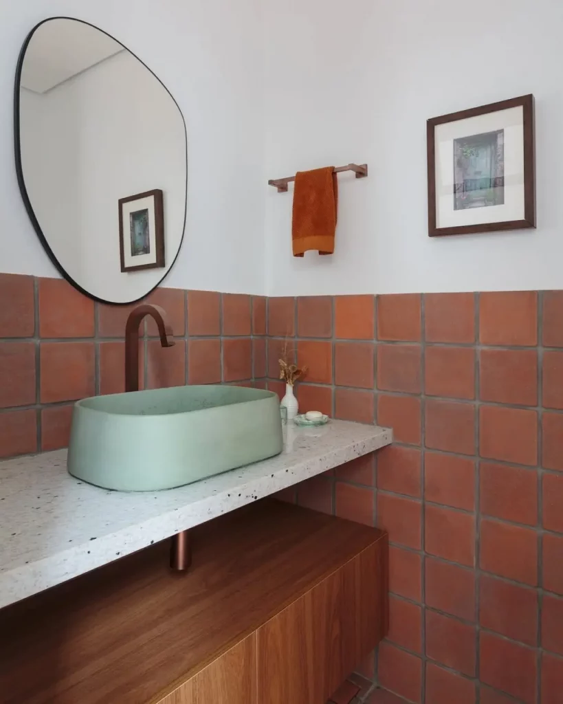 Lavabo com decoração minimalista, quadro simples, espelho orgânico e parede de tijolos.