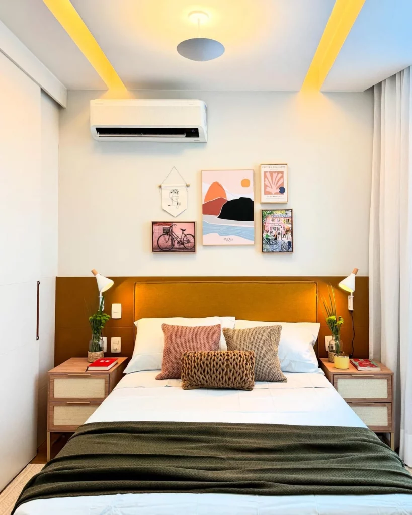 Quarto de casal aconchegante, com parede adornada com quadros, pintura segmentada marrom e cama com almofadas texturizadas de tons diferentes.