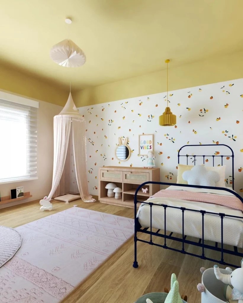 Quarto infantil de menina, delicado, com papel de parede floral, teto e parte da parede pintado em um amarelo esverdeado, cama com grades de metal e cabaninha rosa no fundo.