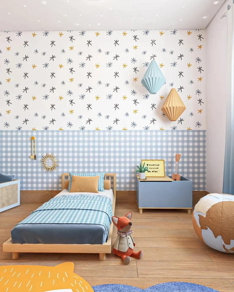 Quarto infantil masculino com dois tipos de papel de parede, sendo um colorido e outro xadrez de azul. Há brinquedos no chão, balões de papel na parede e uma mesa de cabeceira azul perto da cama baixa.