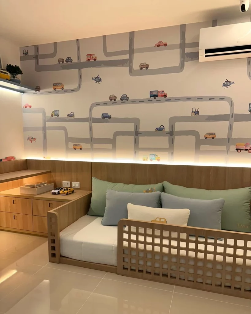 Quarto infantil de menino com papel de parede de pista de carrinhos, cama baixa com muitas almofadas azuis e grade de madeira.