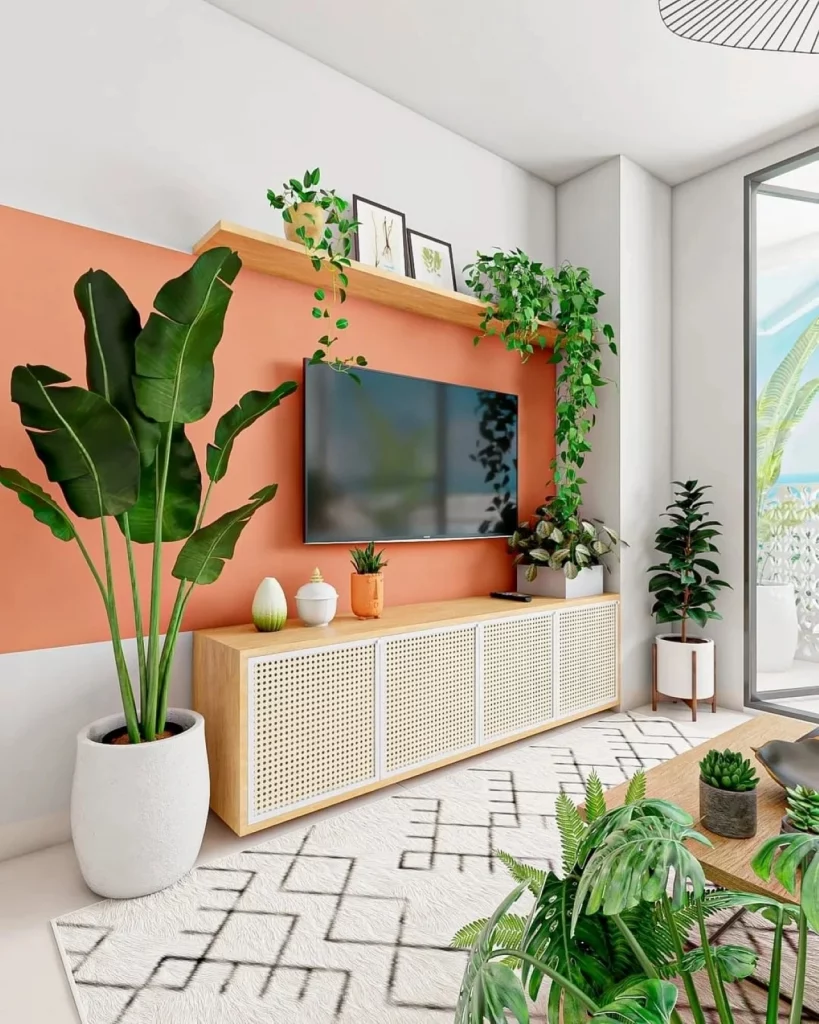 Sala de televisão com pintura segmentada no meio na cor laranja, também há vasos de plantas na lateral do aparador e uma prateleira na parede que apoia trepadeiras e quadros.