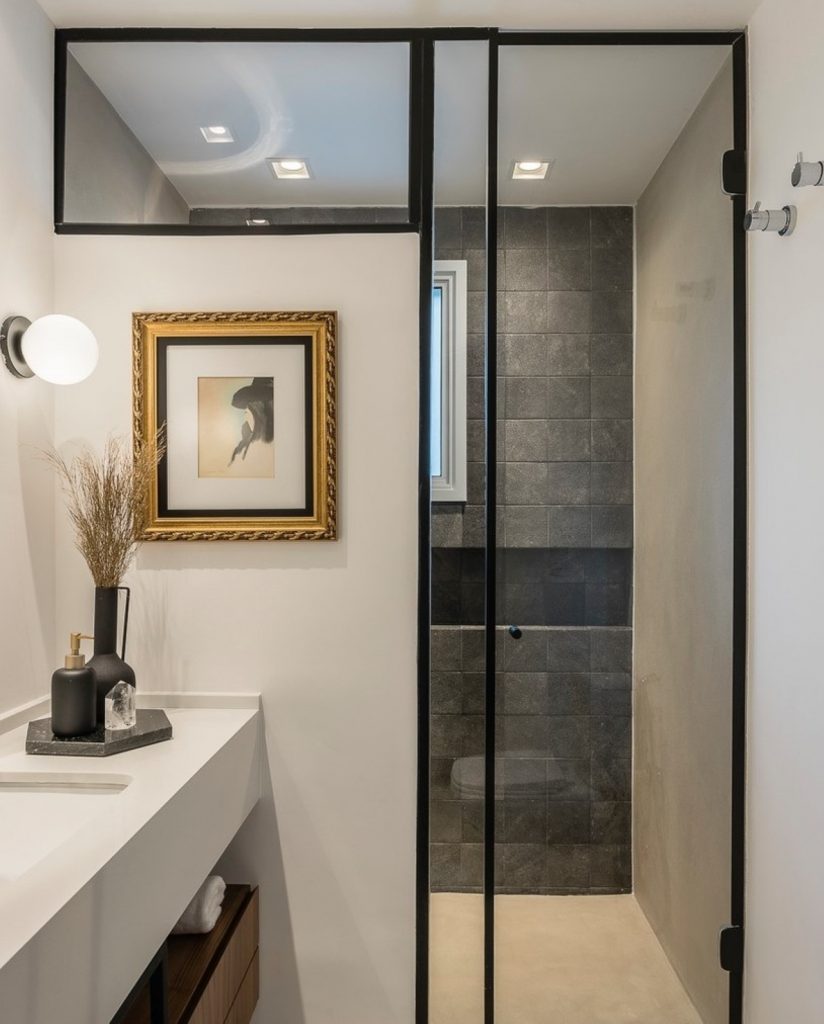 Banheiro moderno com box diferente e detalhes em preto, com quadro pendurado na lateral da pia.