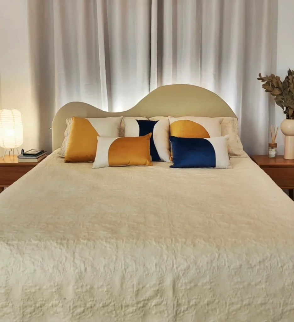 Cama com cabeceira iluminada em luz fria e branca, almofadas coloridas em amarelo e azul.