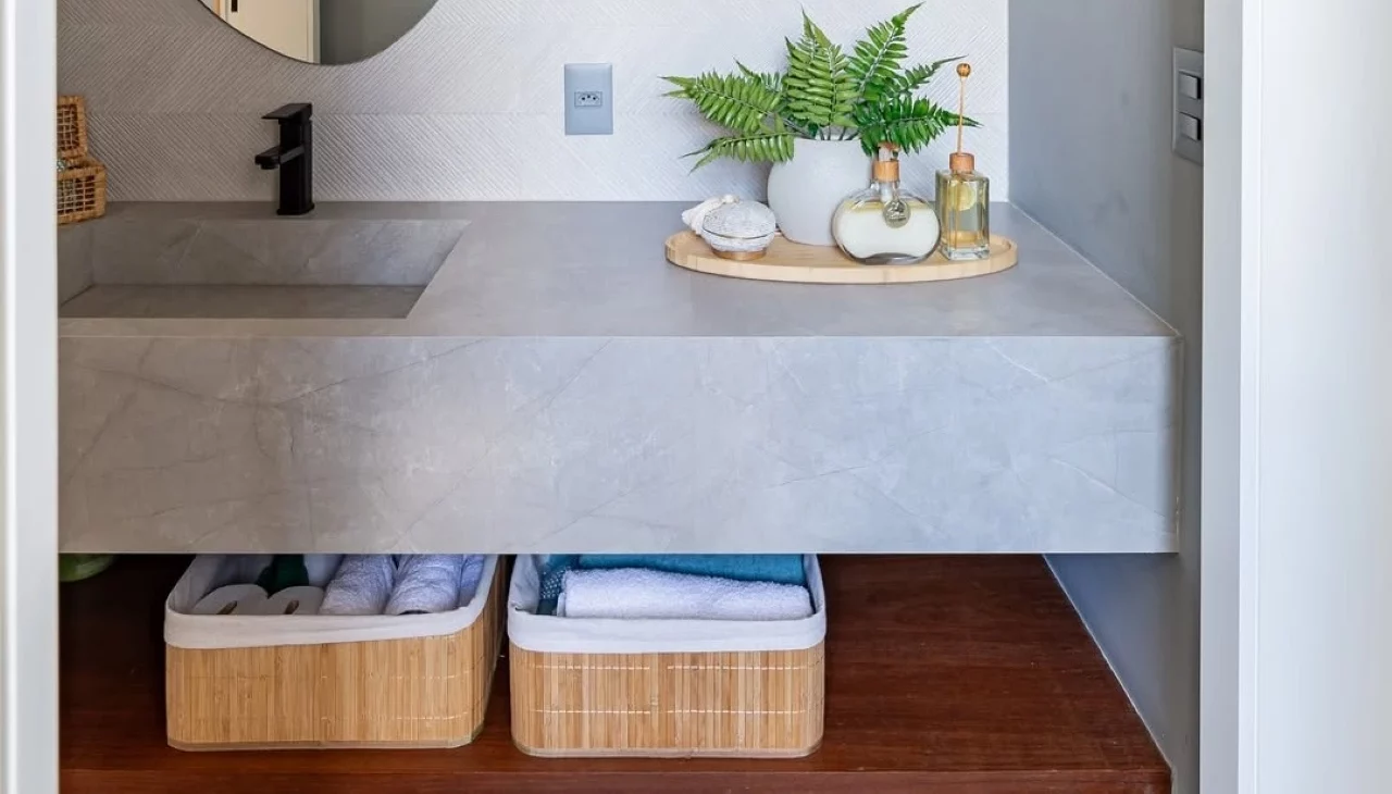 Caixas para organizar papel higiênico e toalhas, bandeja de madeira com vaso de planta, espelho orgânico.