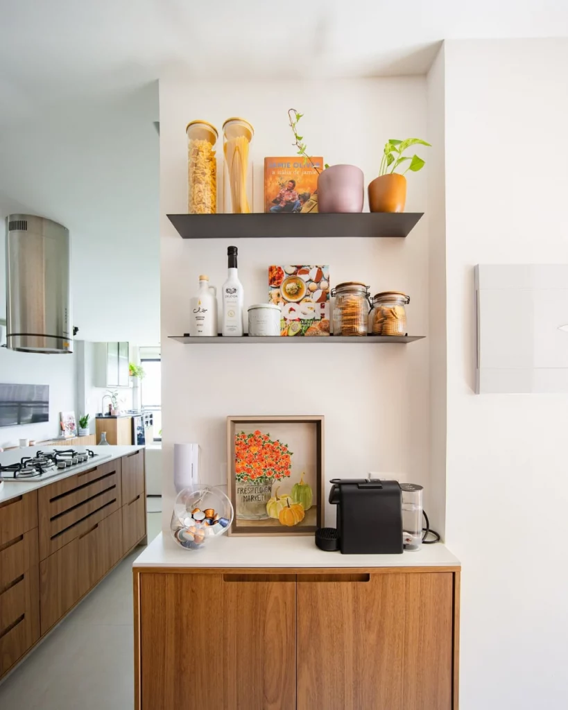 Cantinho do café decorado com objetos em tom de laranja, prateleiras com utensílios e máquina de café no balcão.
