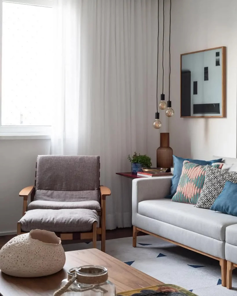 Canto com luminárias pendentes, quadro, sofá e poltrona cinzas.