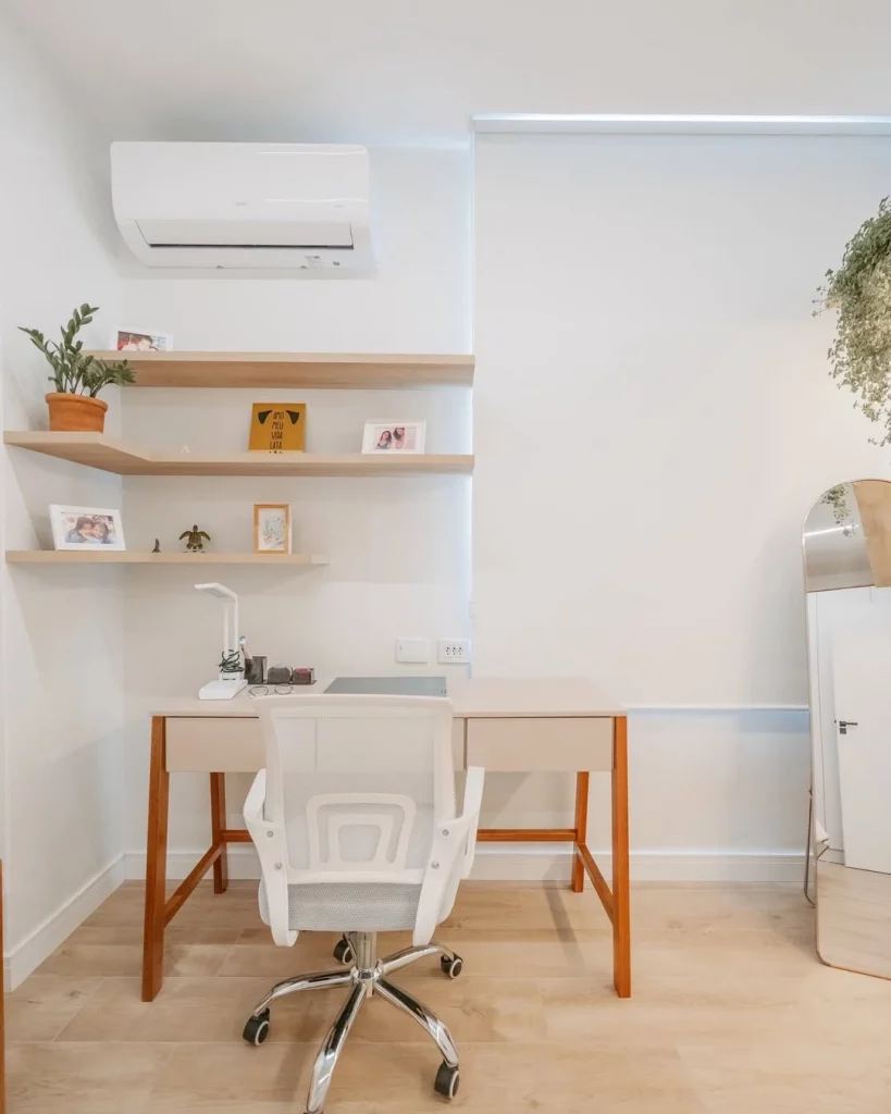 Canto de estudos com mesa, cadeira branca, prateleiras com objetos decorativos e planta.