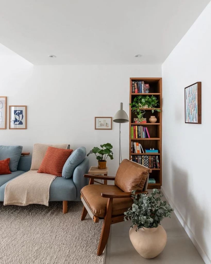 Sala aconchegante, com prateleira de livros, poltrona, sofá azul e manta.