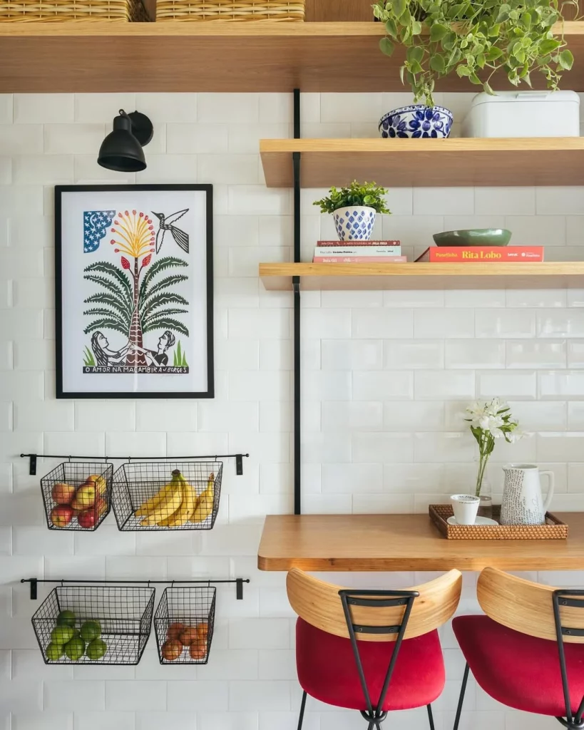 Cantinho na cozinha com mesa dobrável, prateleiras, fruteiras na parede e quadro.