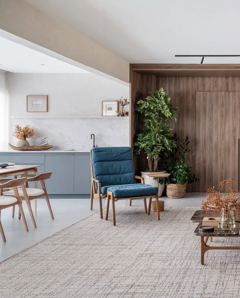 Sala com poltrona azul escuro, parede de madeira e plantas no canto.