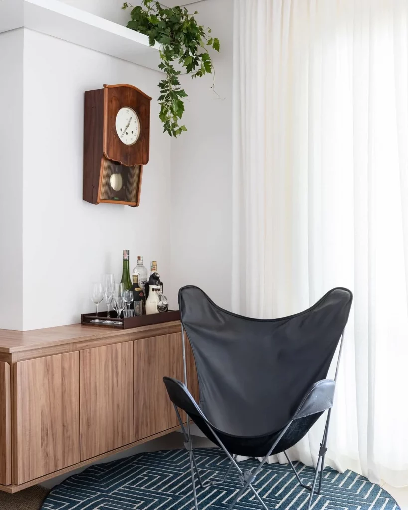 Relógio vintage decorando o canto da parede, com planta e poltrona preta.