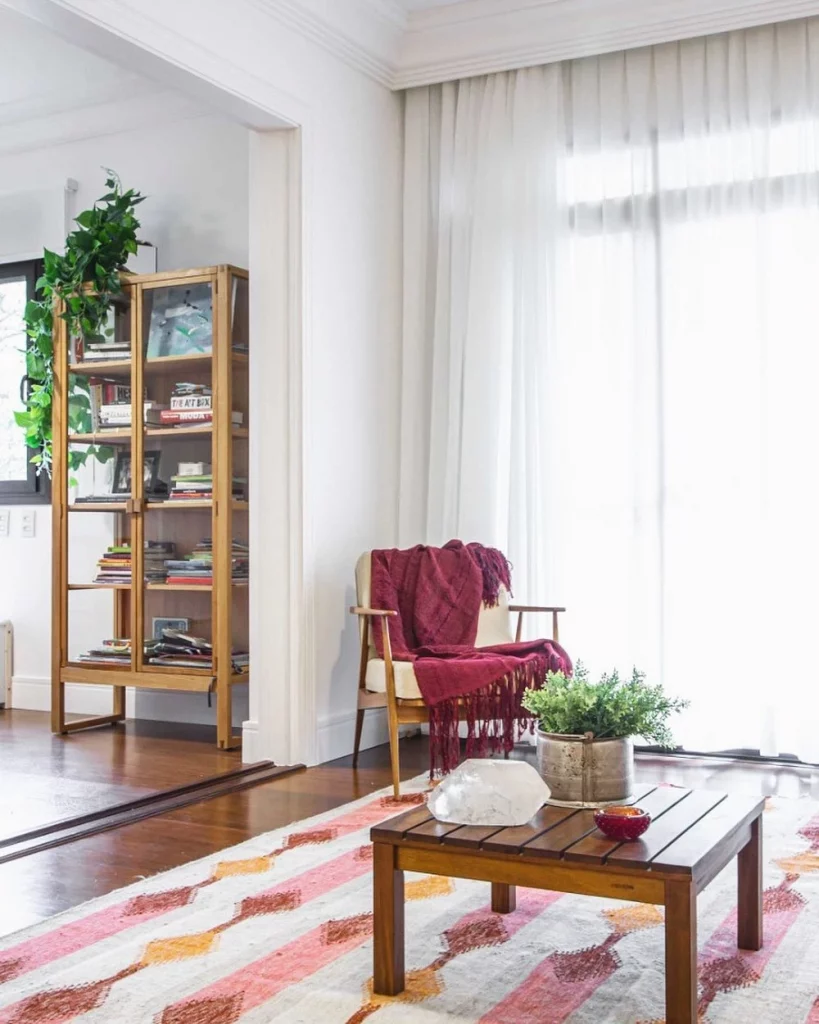 Cantinho da leitura com poltrona, manta bordô e estante com livros e plantas.