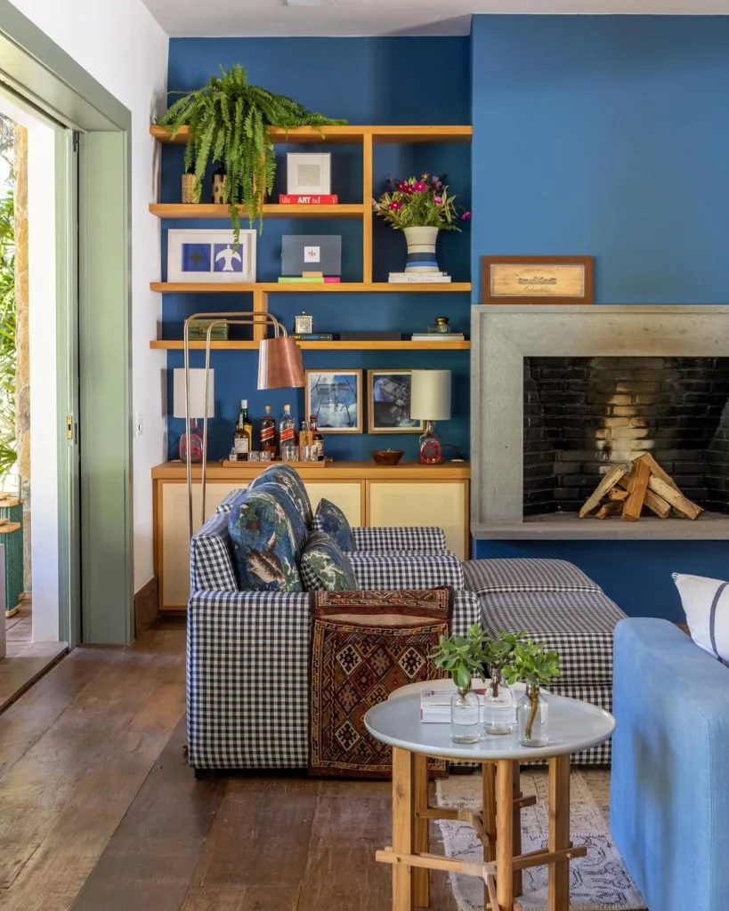 Prateleiras com diversos itens decorativos, quadros, plantas, sofá xadrez e mesa lateral.