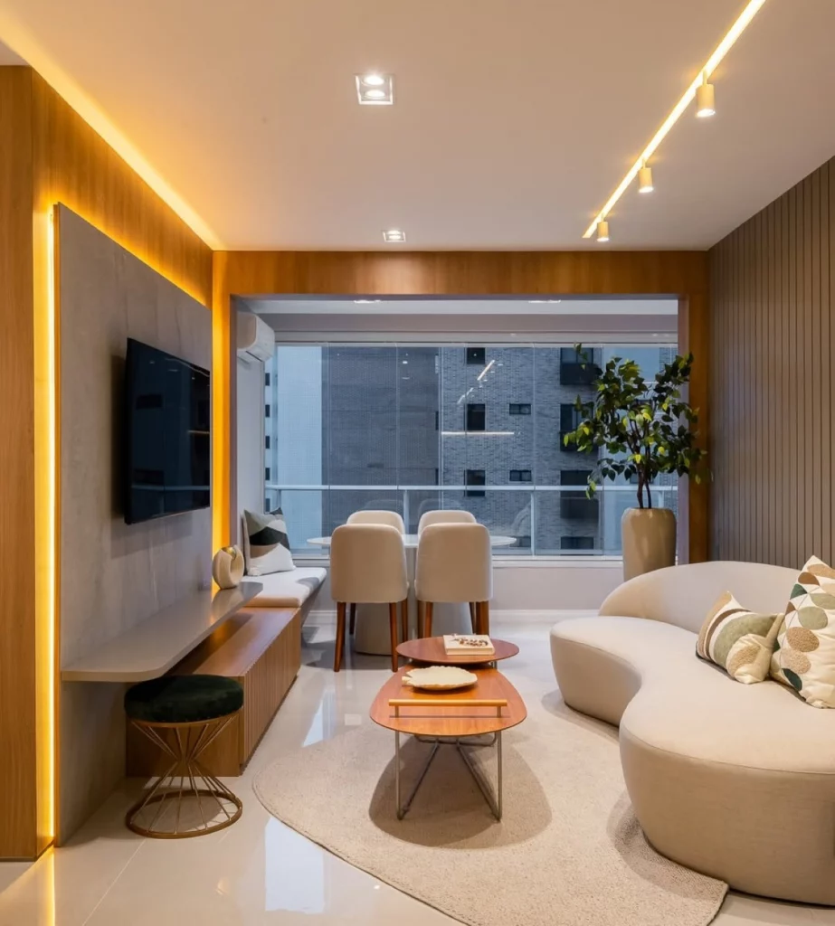 Sala de estar com televisão, sofá moderno, mesa de centro de madeira e iluminação amarela em fitas de led e spots.