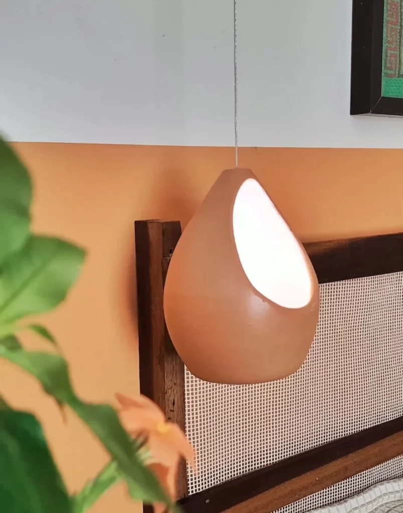 Luminária feita com vaso de plástico diferente, assemelhando-se a vaso de barro, com luz branca dentro.
