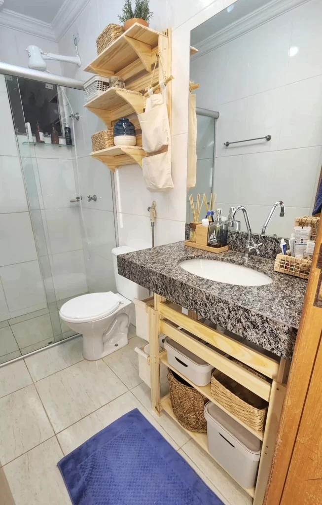 Banheiro com móveis feitos de madeira embaixo da pia e acima do vaso sanitário.