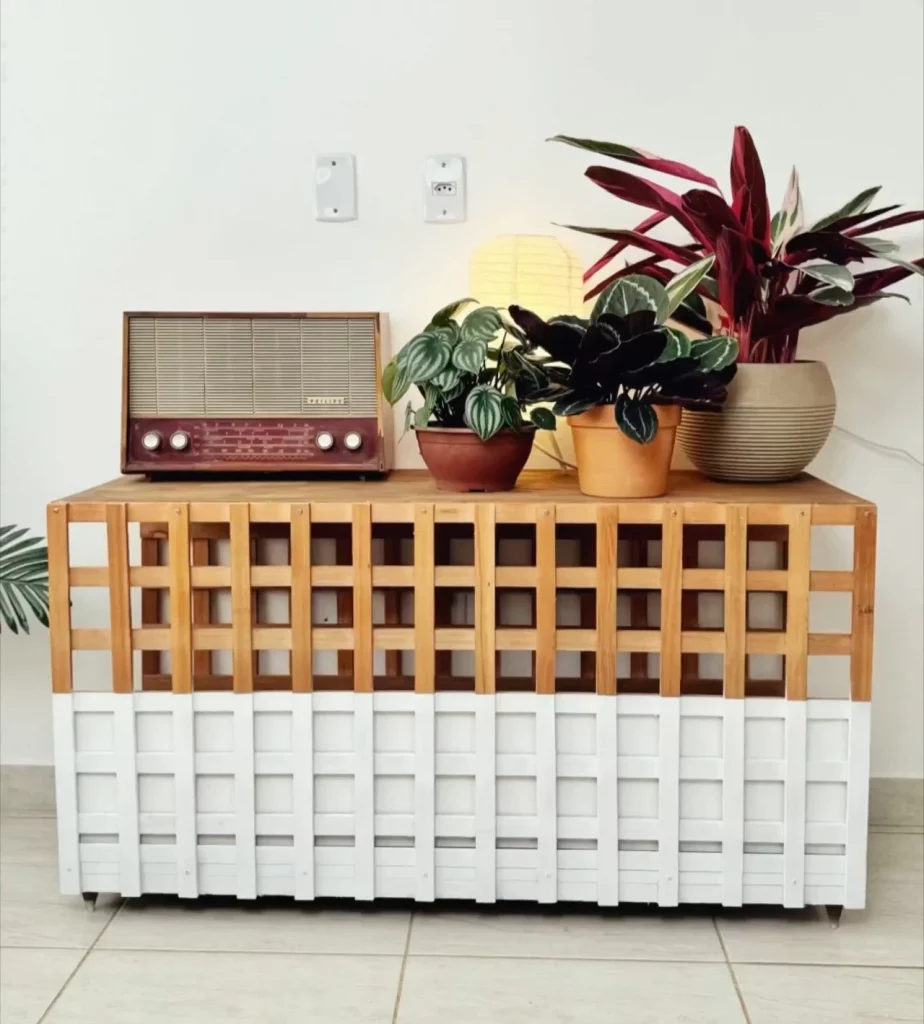 Móvel de madeira com metade da frente pintada de branco, vasos de plantas no tampo e rádio antigo.