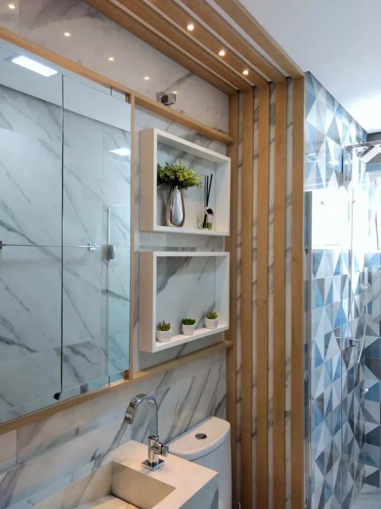 Banheiro com dois nichos brancos na parede, ao lado do espelho, parede de mármore e azulejos geométricos na parte interna do box junto de uma divisória de madeira.