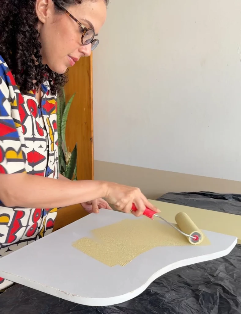 Pintando tampo da mesa branco de amarelo com rolo de tinta.