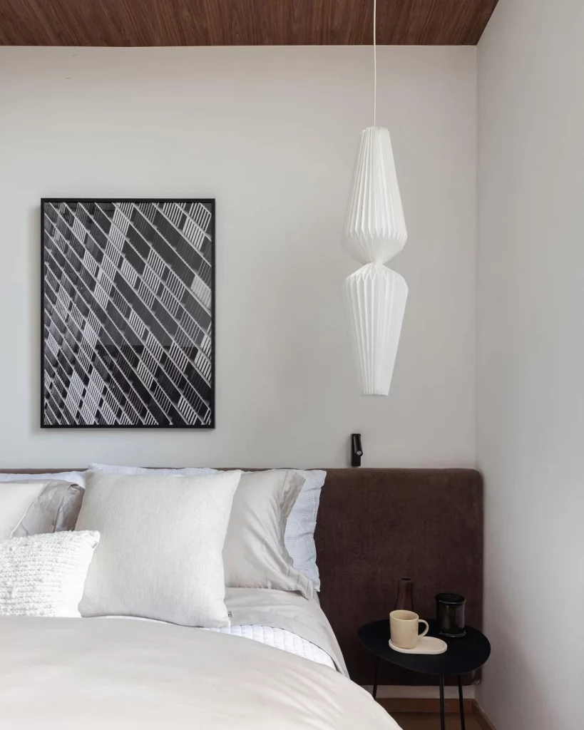 Quarto com visual moderno e sóbrio, com cabeceira marrom escuro e quadro na parede branca.