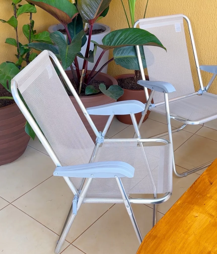 Cadeiras de praia na cor brancas com plantas no fundo.