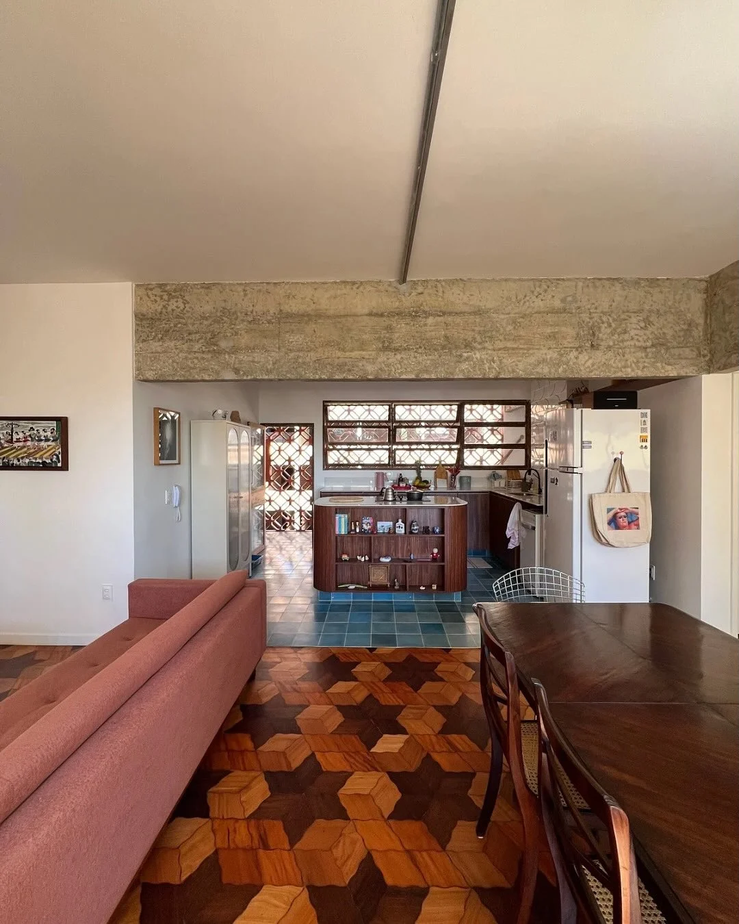 Móveis em tom de marrom escuro e piso com detalhes na mesma cor, sofá goiaba e parede com objeto pendurado.