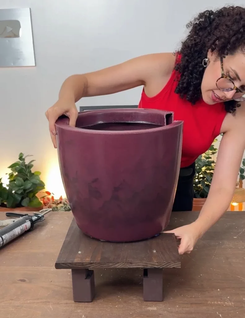 Vaso de planta roxo sendo encaixado na prateleira de madeira com pés.