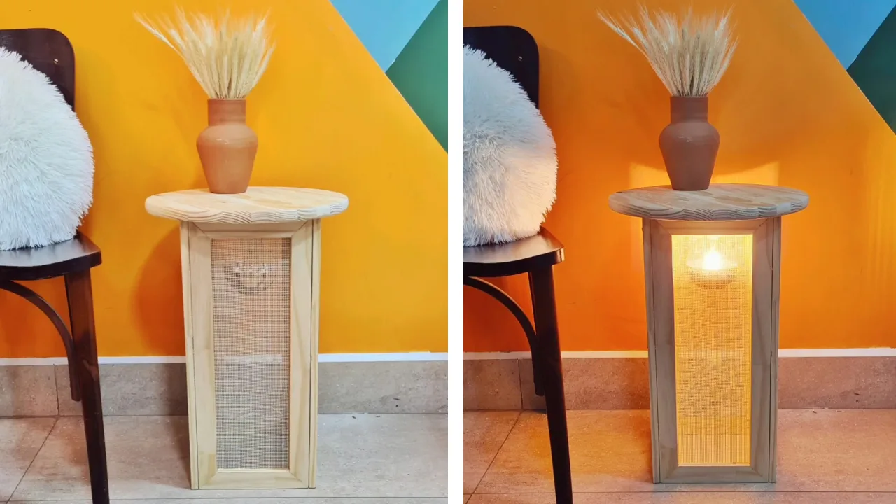 Mesa de cabeceira feita com ripa de madeira e talagarça com iluminação de luz amarela e vaso de ramos secos.