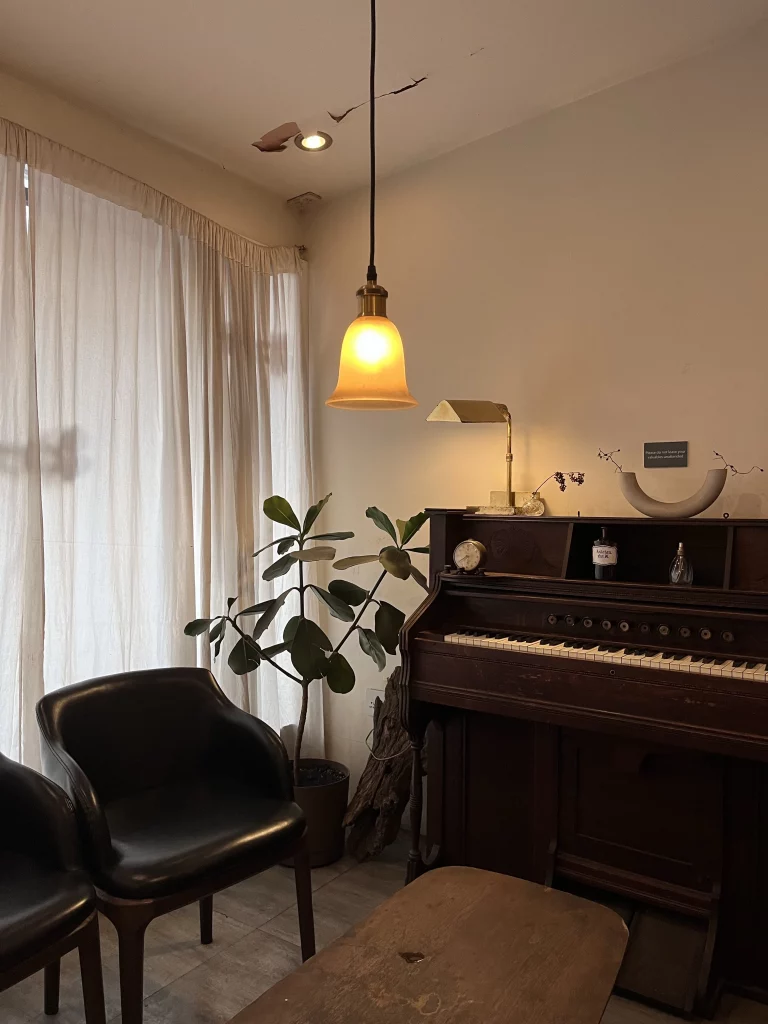 Sala com luz amarela, piano de madeira escura e poltrona marrom com planta no fundo.