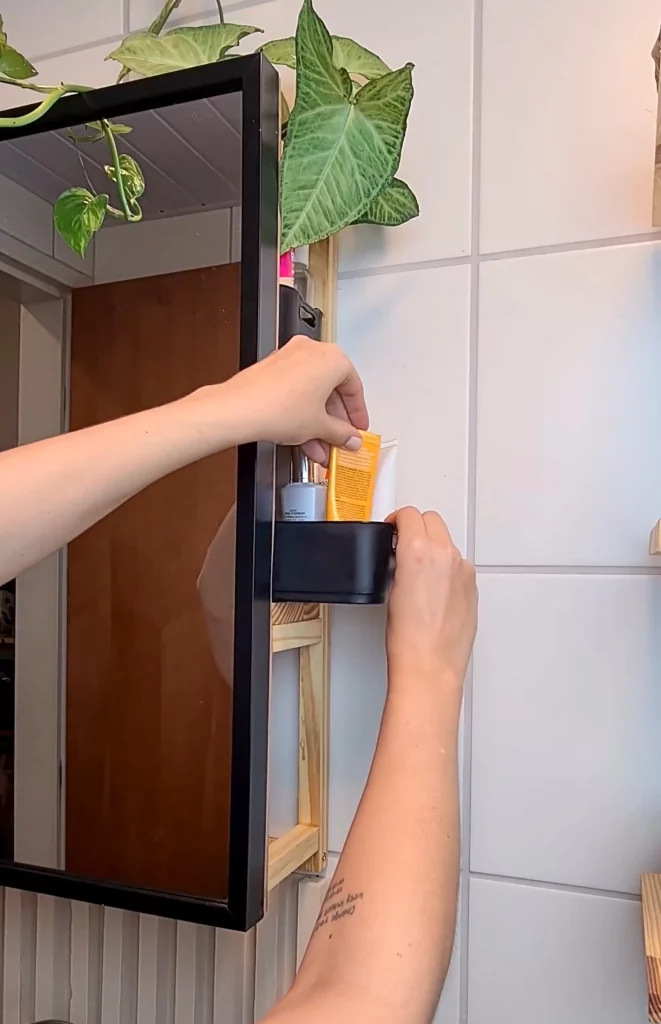Colocando itens de higiene pessoal e autocuidado na prateleira embutida no espelho.