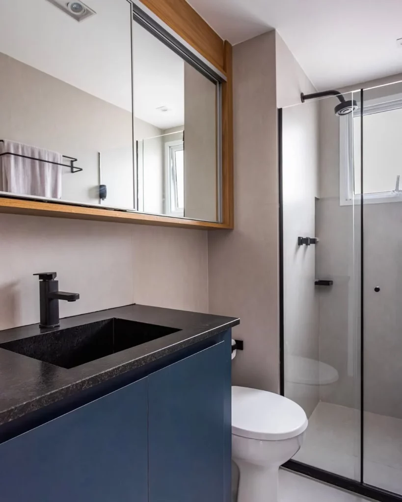 Banheiro com tons de azul marinho e pia preta, visual sóbrio.