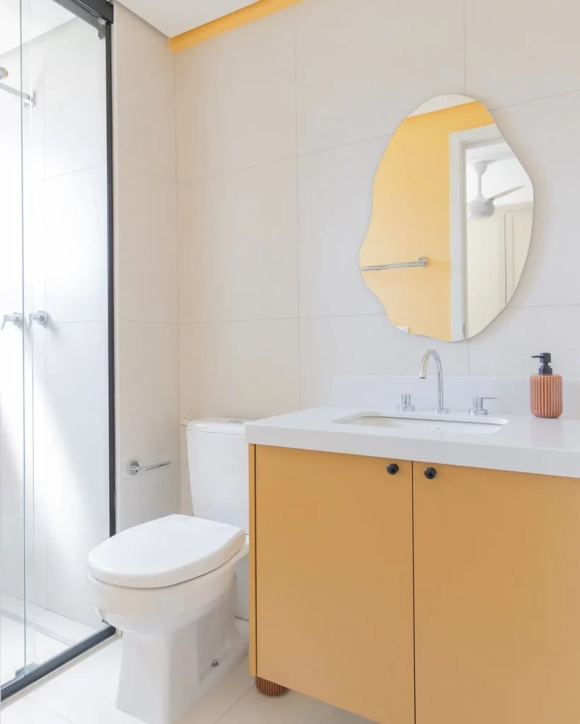 Banheiro com armário laranja e espelho orgânico.