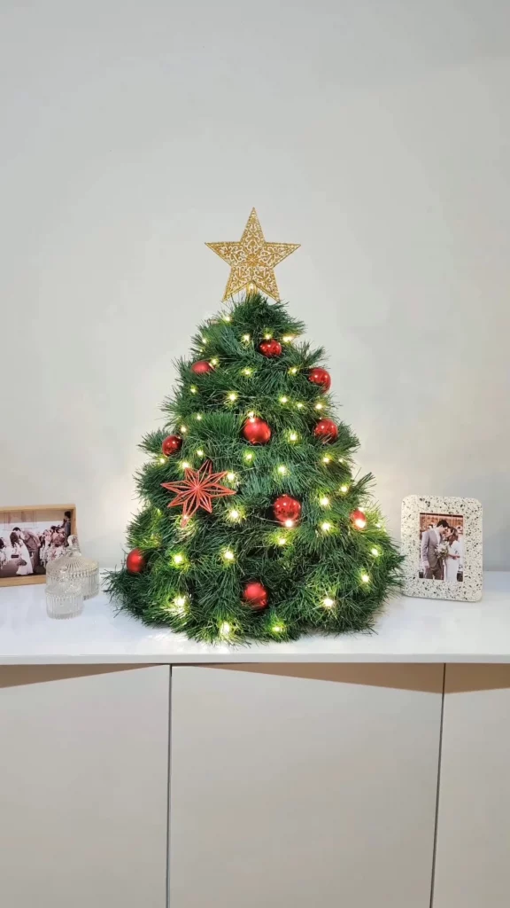 Árvore de natal feita com guarda-chuva, decorada com bolinhas vermelhas e fio de fada de luz amarela.