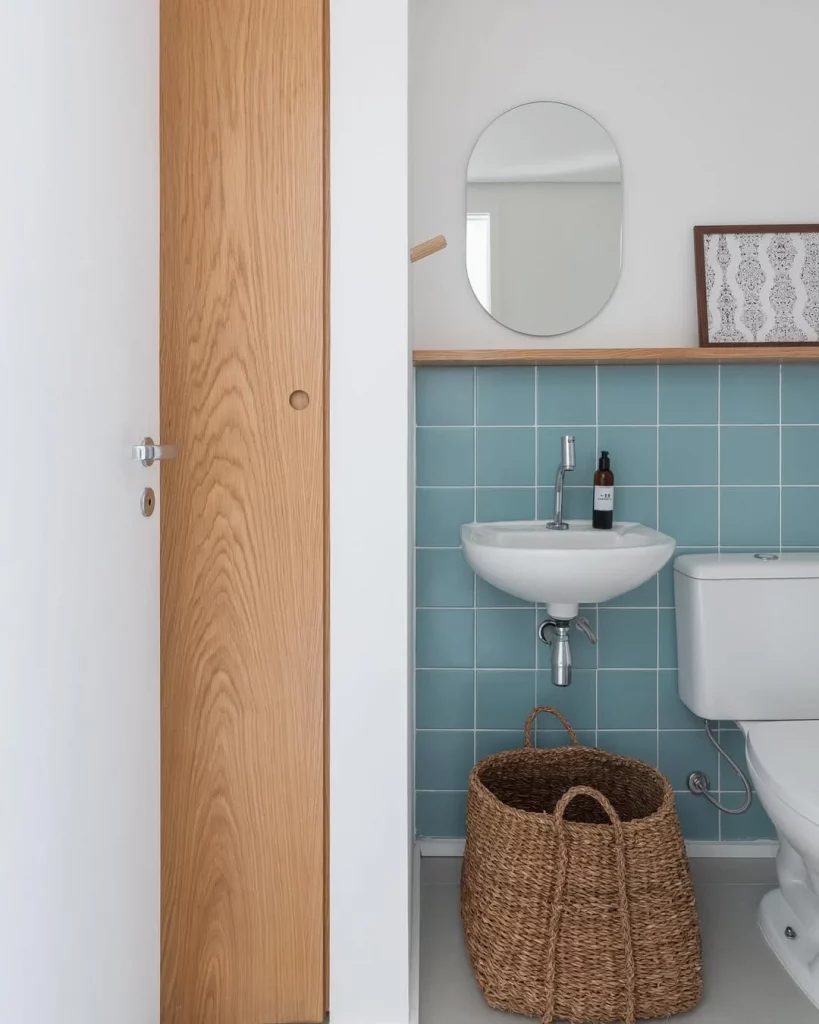 Banheiro com revestimento azul, cesto de palha e quadro na parede.