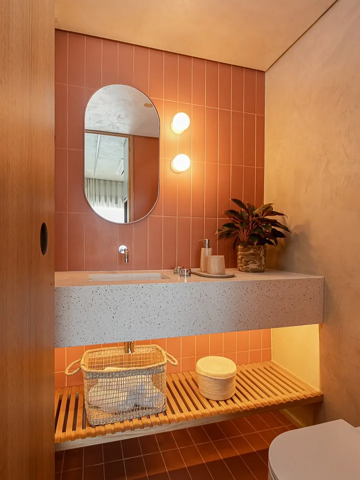 Banheiro com revestimento terroso e avermelhado e iluminação na lateral do espelho.