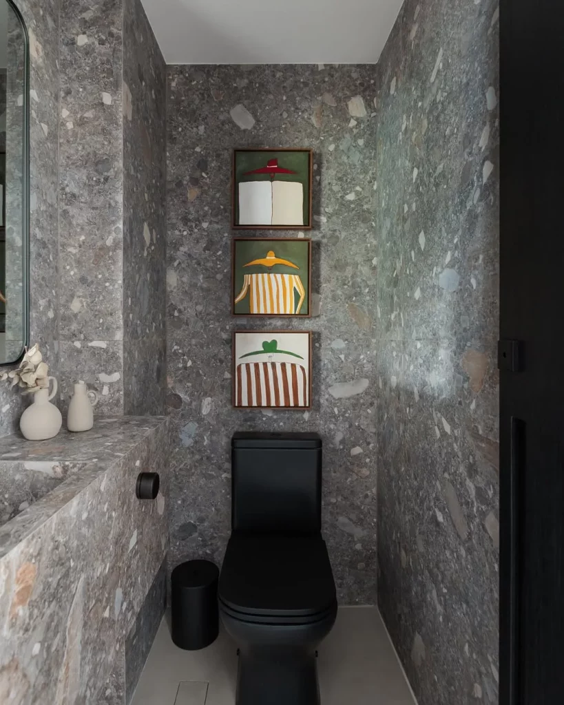 Banheiro cinza escuro com vaso preto e quadros na parede.