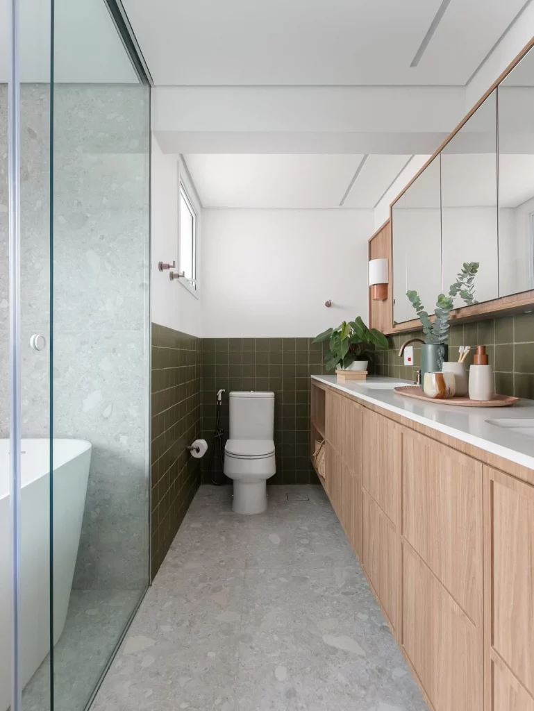 Banheiro com azulejo verde escuro, armário de madeira e piso de porcelanato acetinado cinza.