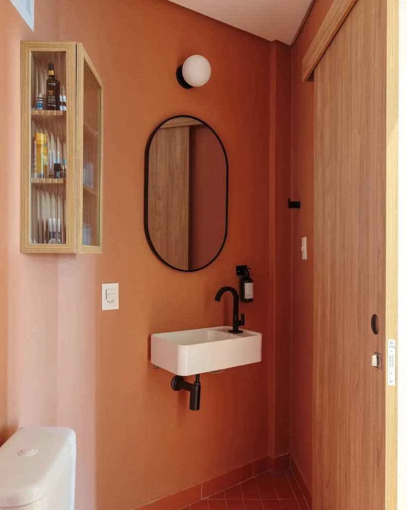 Pintura laranja terroso no banheiro com espelho de moldura preta.
